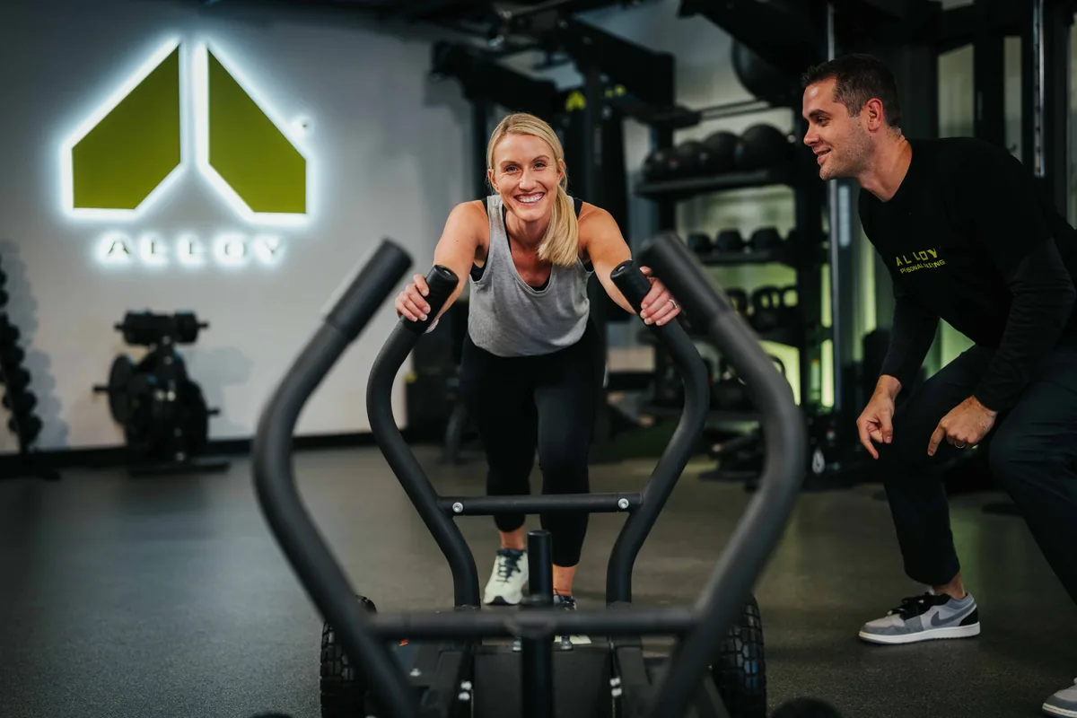 Alloy Personal Training coach guiding a member through a sled push
