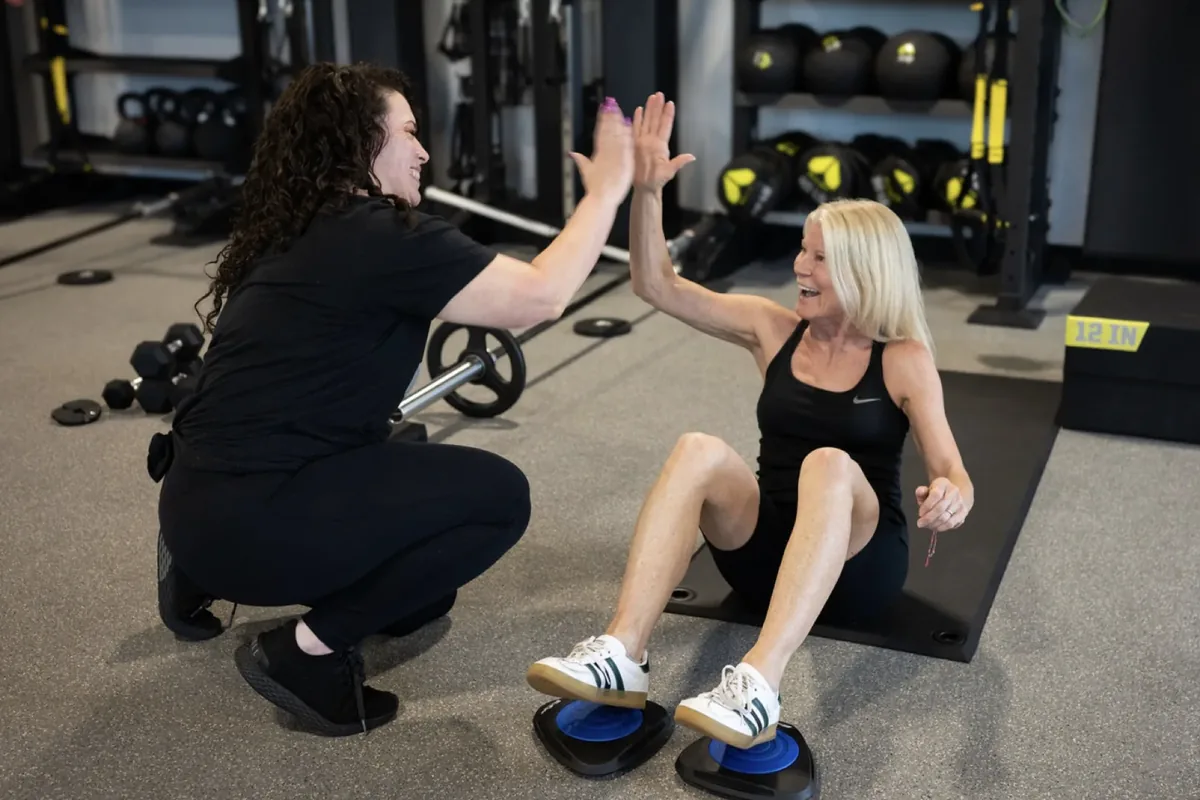 A coach high-fives a member mid-exercise during a coached session on the training floor at an Alloy Personal Training studio