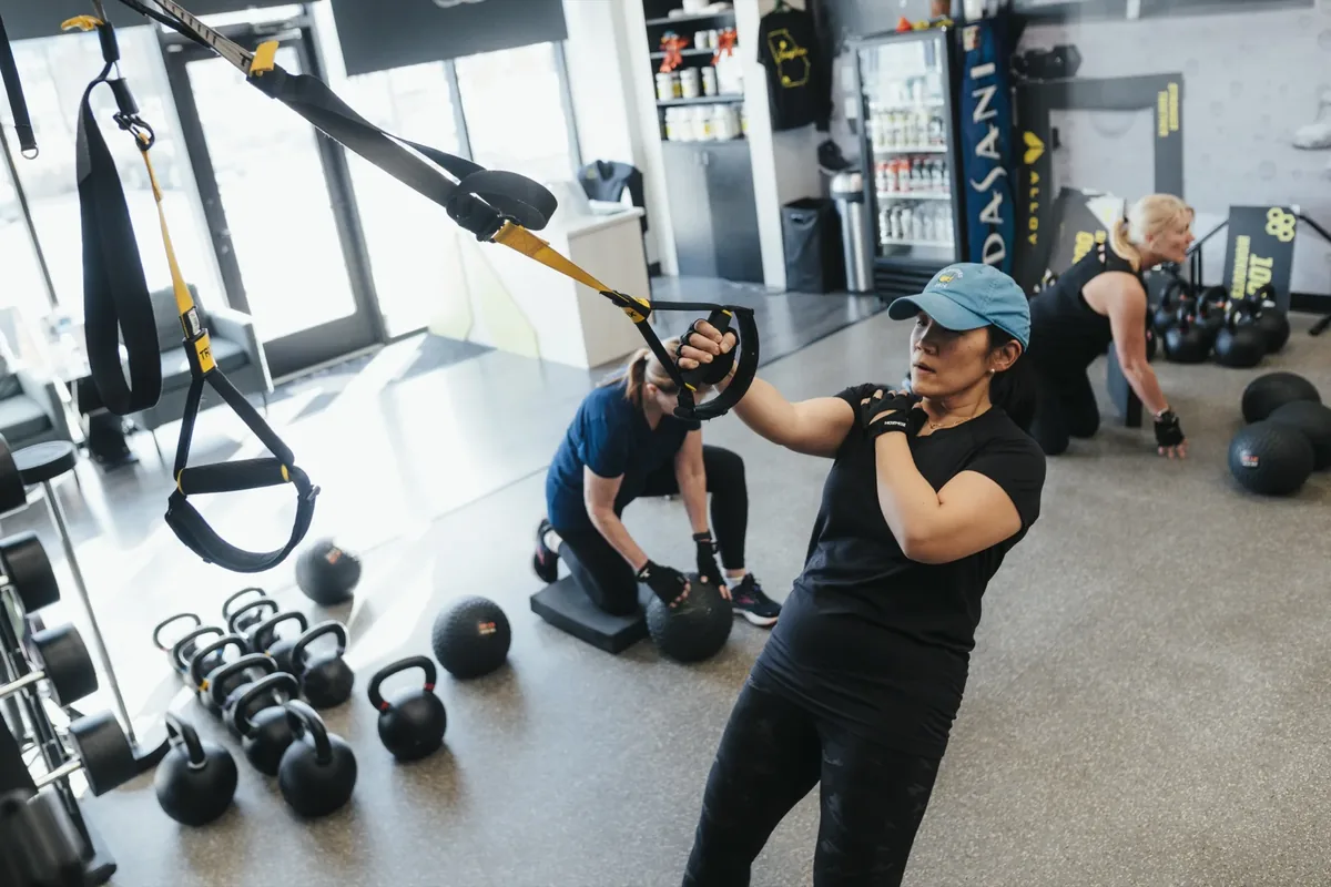 Three women work through a small group training session with TRX straps and slam balls at an Alloy Personal Training studio