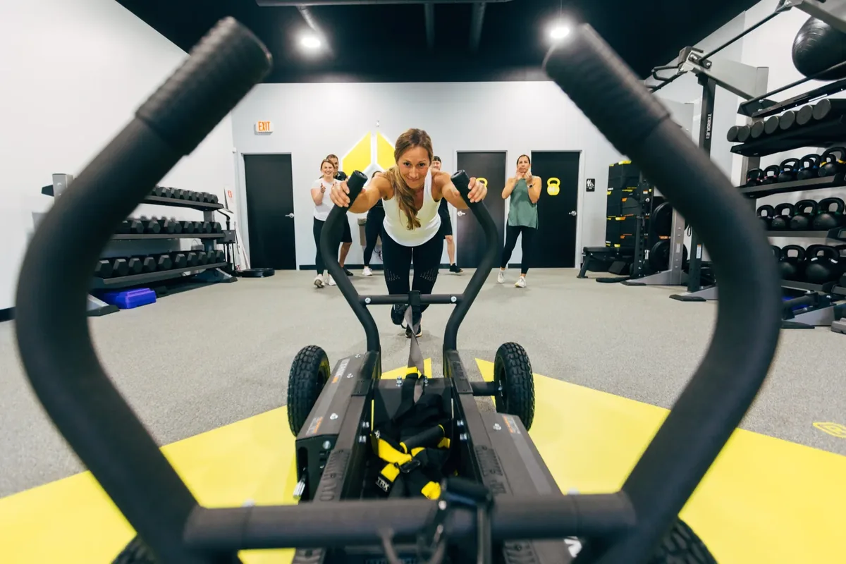 A member pushes a weighted sled while her small group cheers her on at an Alloy Personal Training studio