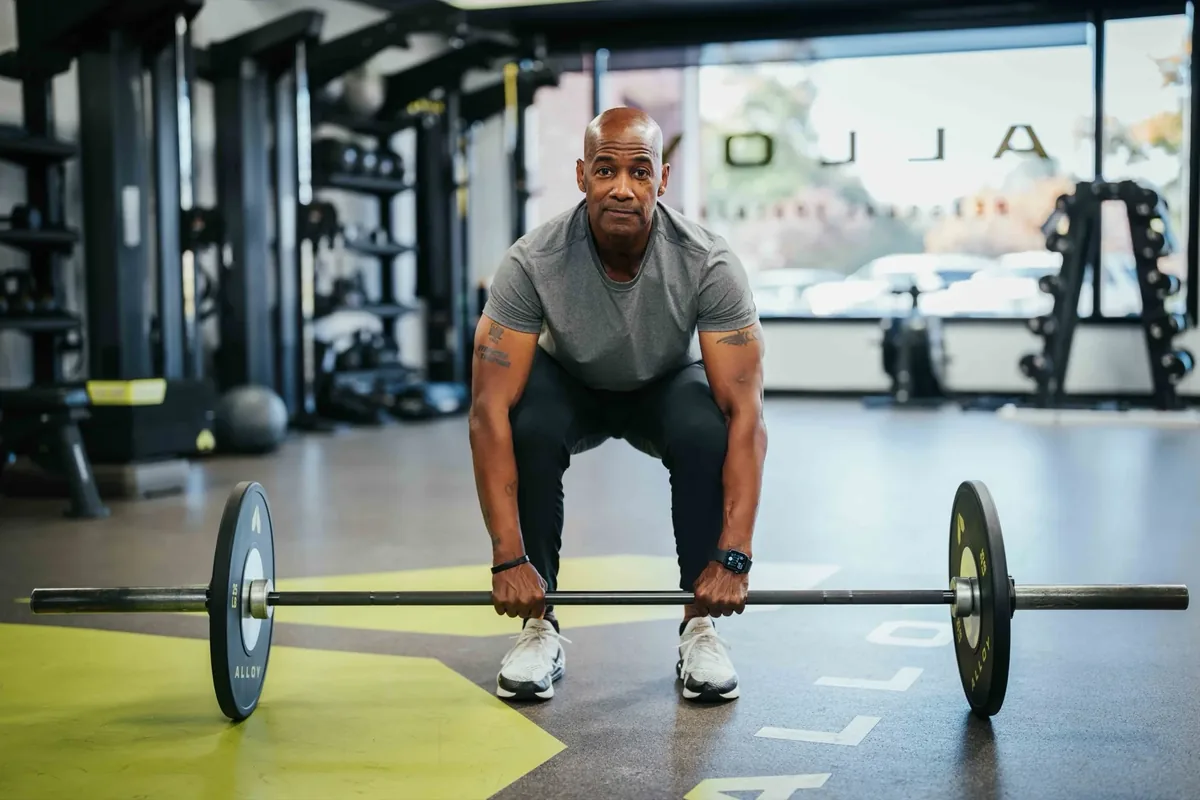 A member in his 50s sets up to deadlift a barbell during a coached session at an Alloy Personal Training studio