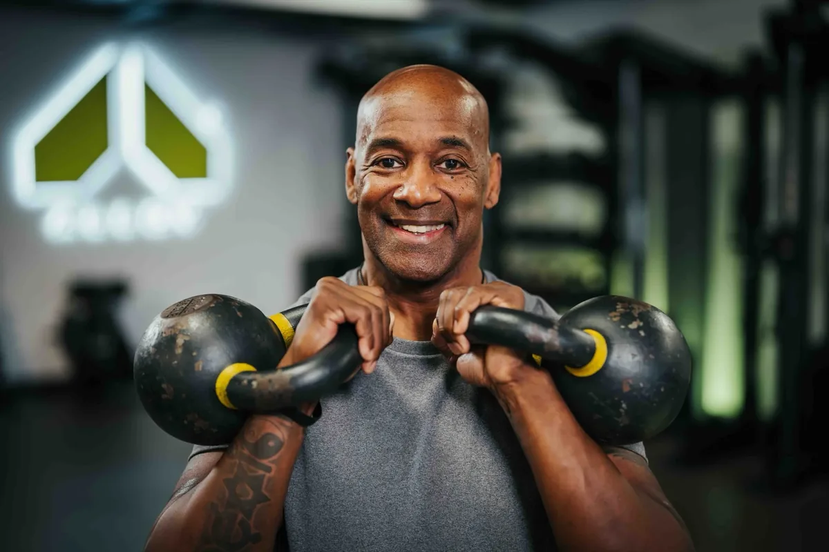A member holds a pair of kettlebells in the rack position during a coached session at an Alloy Personal Training studio