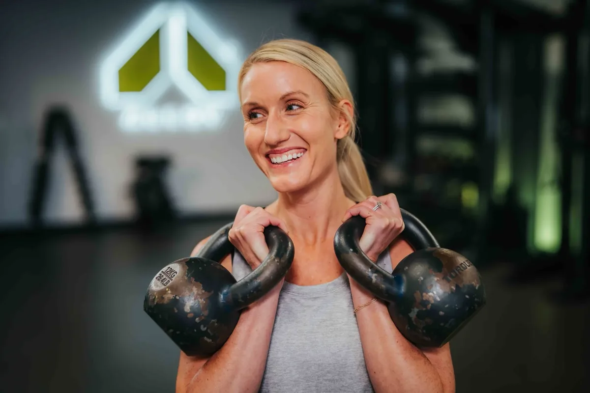 A member pauses with two kettlebells racked before her next set at an Alloy Personal Training studio