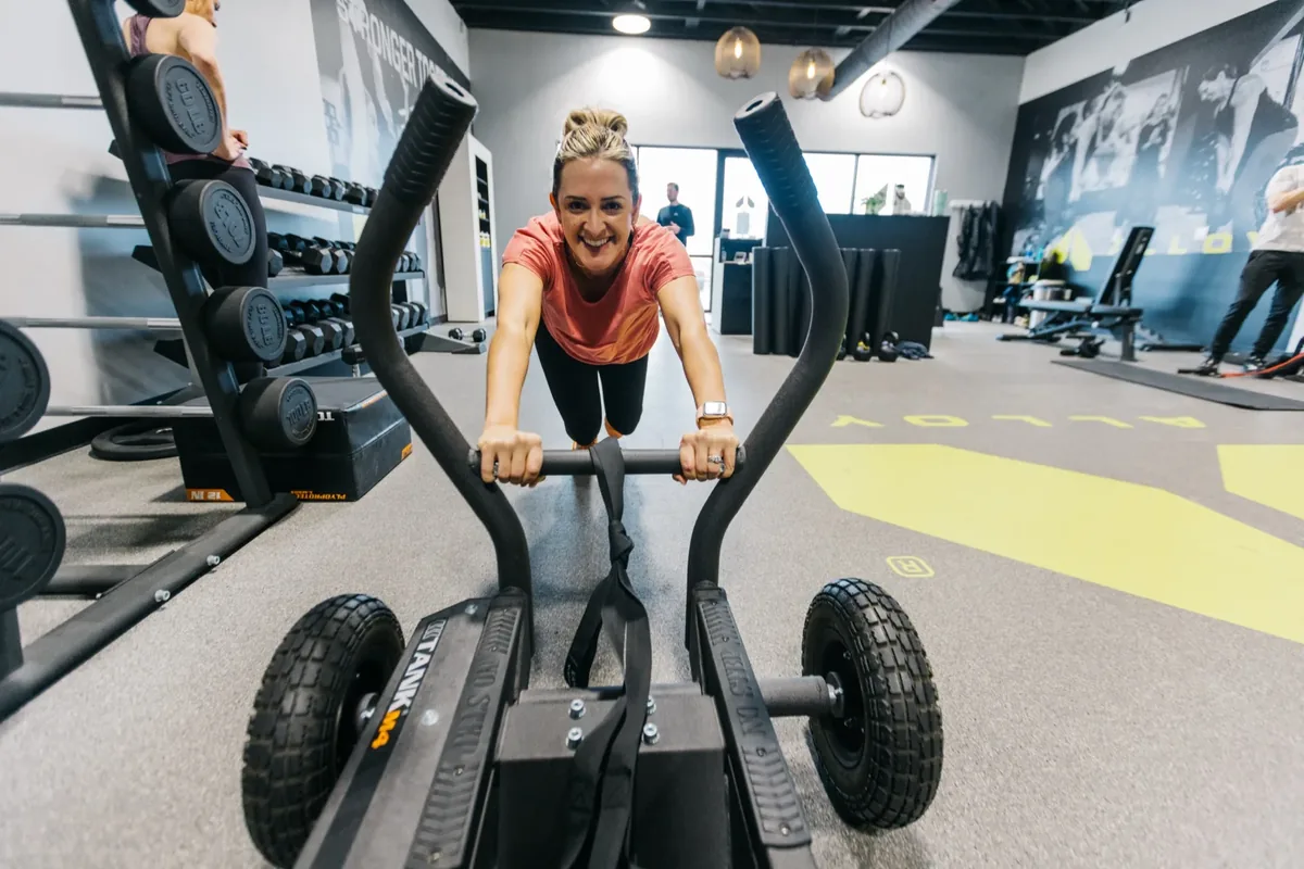 A member pushes a training sled across the floor during a timed block at an Alloy Personal Training studio